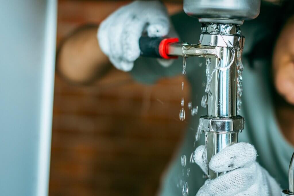 Gloved hands tightening a leaking chrome pipe